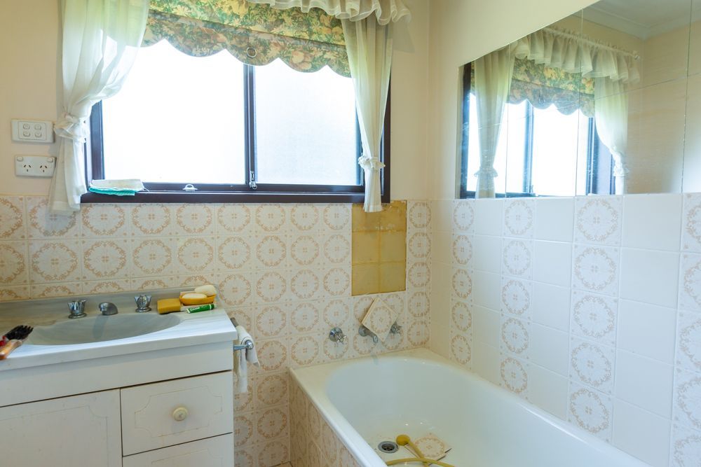 Bathroom with a white vanity, bathtub, window, and a frosted glass shower door.