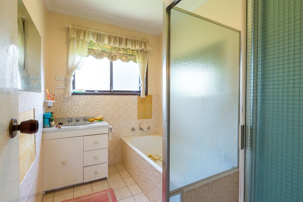 Bathroom with a white vanity, bathtub, window, and a frosted glass shower door.