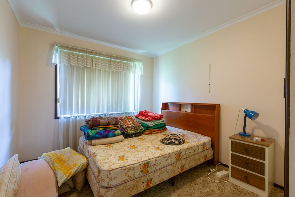 Living room interior with brown sofa, rug, and wooden desk near window with blinds.