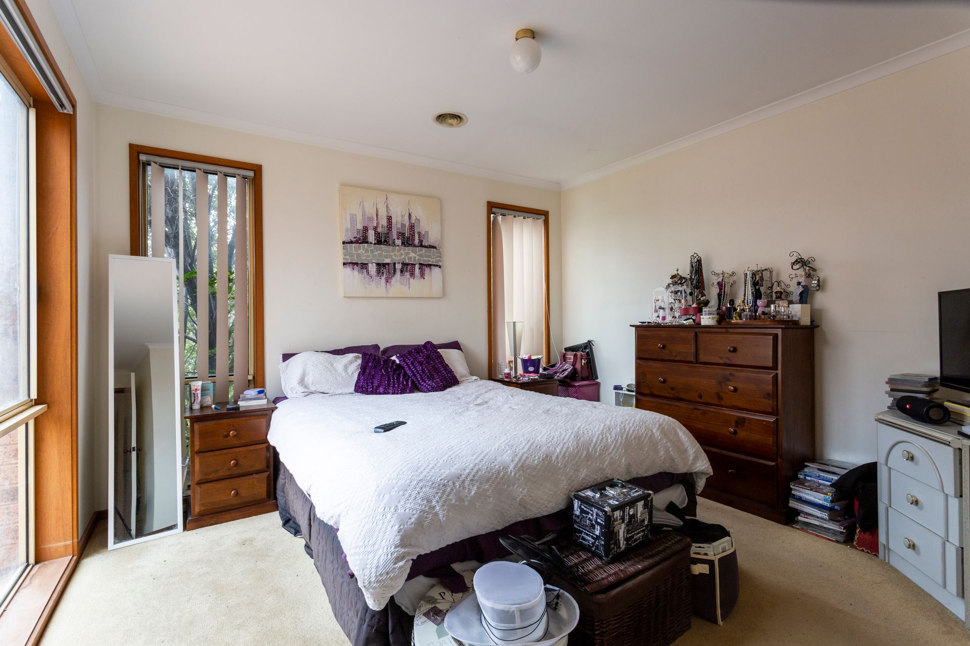 Cluttered living room with furniture, boxes, and a wooden bookshelf, with a window and a red chair.