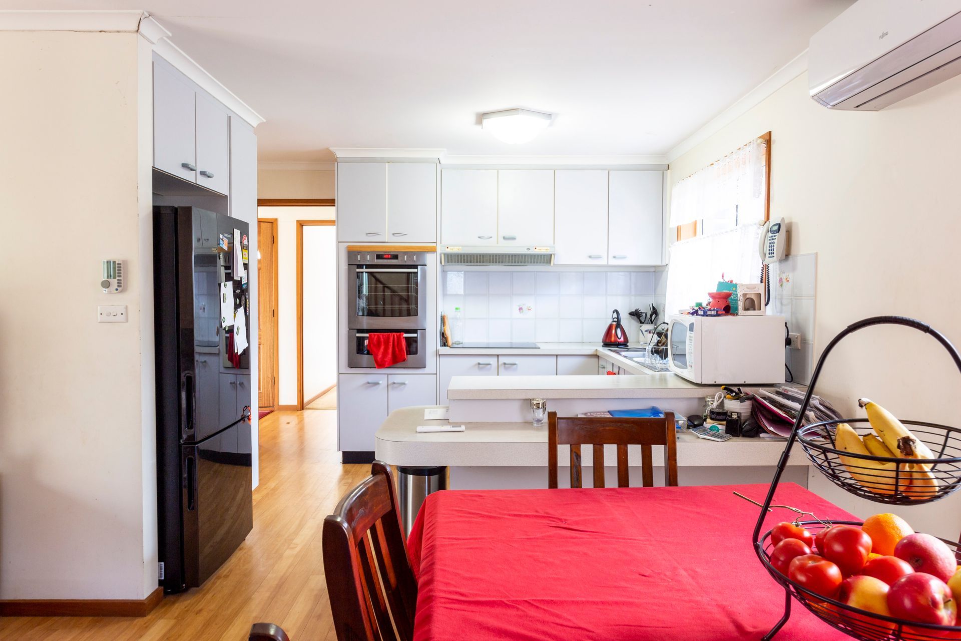 Kitchen with white cabinets, black refrigerator, red table setting, and fruit basket.