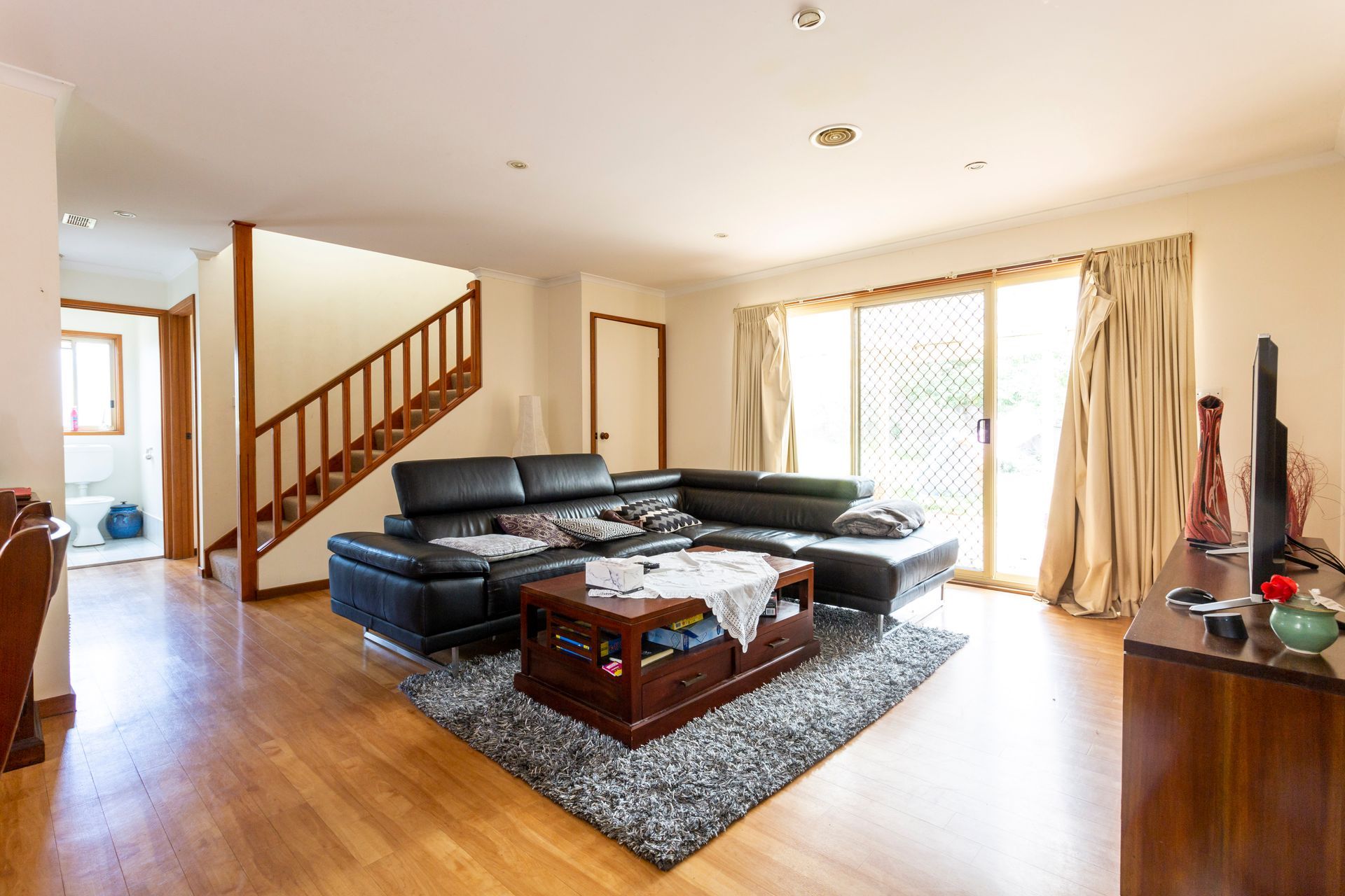 Living room with black sectional sofa, hardwood floors, stairs, and sliding glass door.