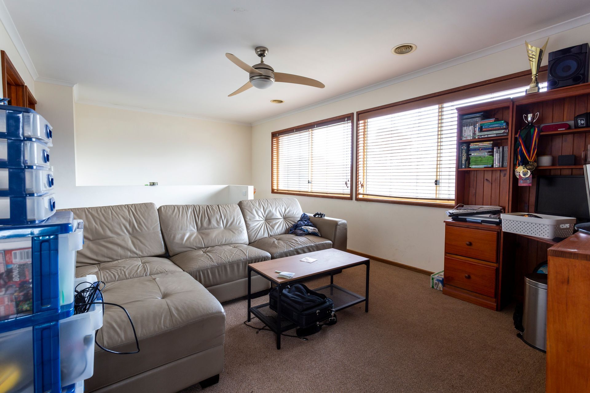Cluttered living room with furniture, boxes, and a wooden bookshelf, with a window and a red chair.