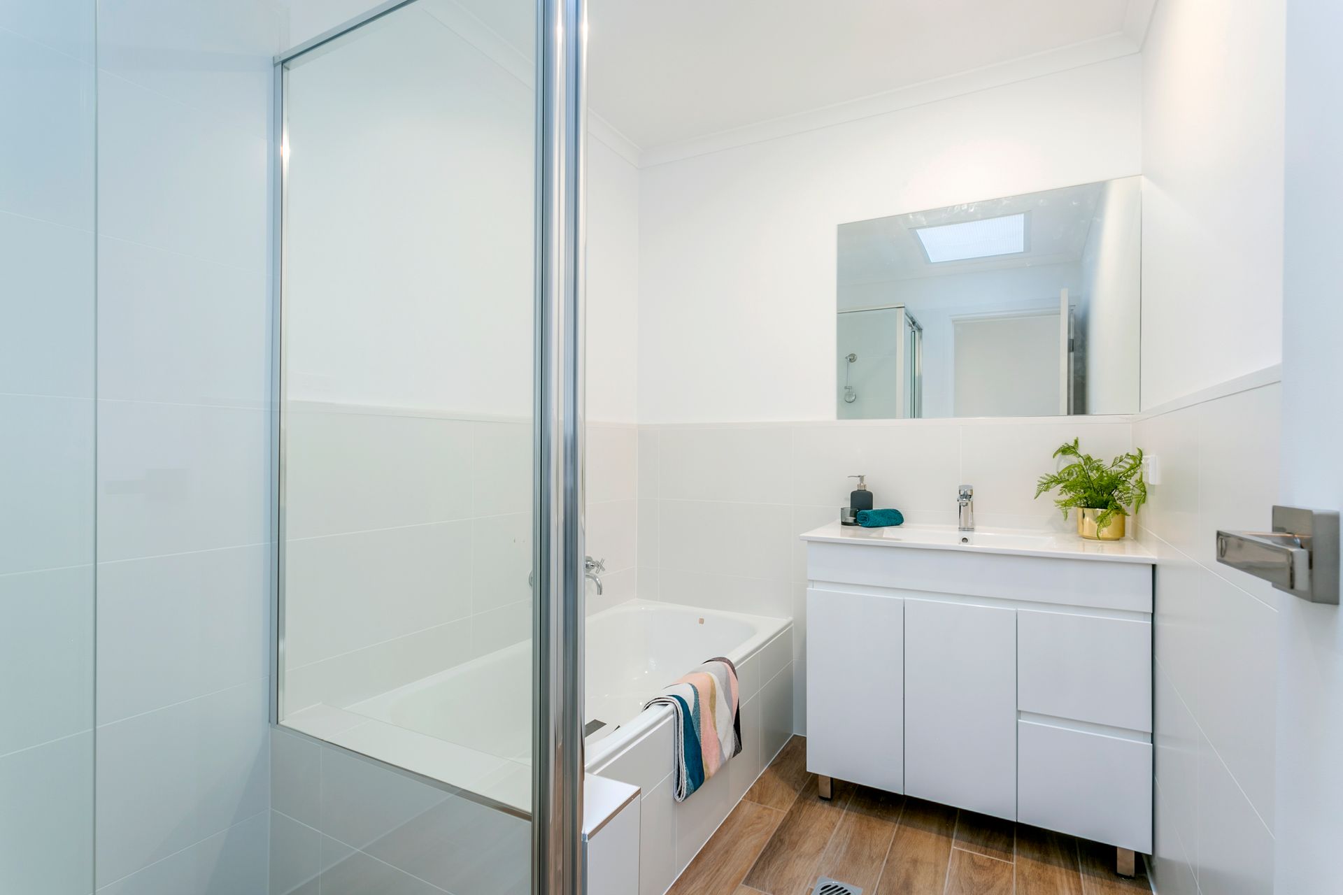 White bathroom with a bathtub, glass shower door, white vanity, and large mirror.