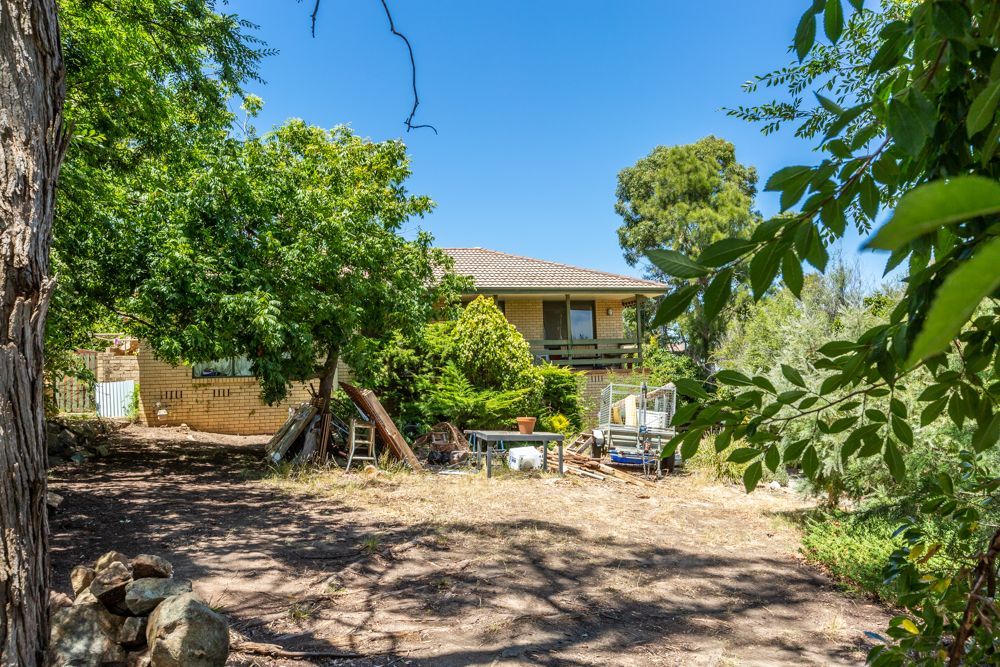 Cluttered dining room with table covered in clothes and items; two framed art pieces on the wall.
