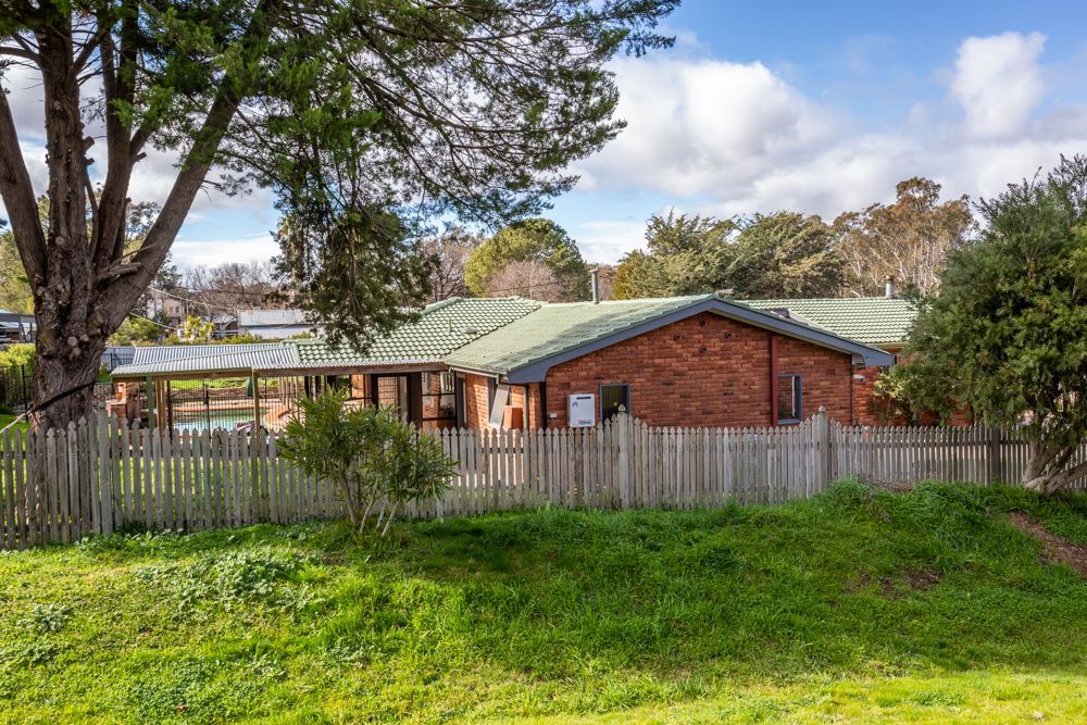 Swimming pool with brick surround, next to a brick house under a blue sky.