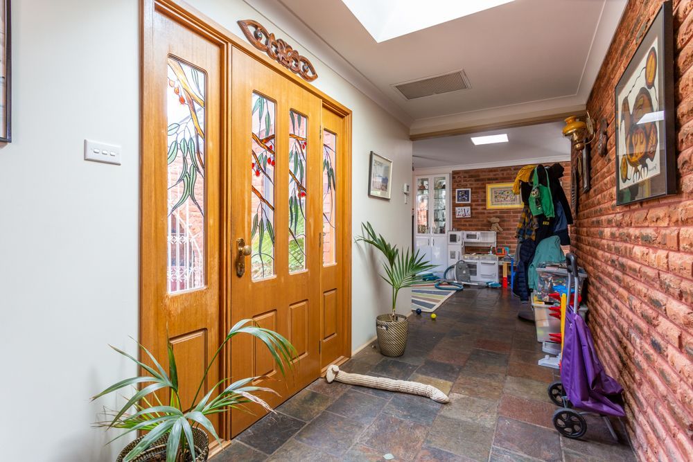 Bathroom with shower, vanity, and bathtub. Plants hang near the window and mirror. Light-colored tile and cabinets.