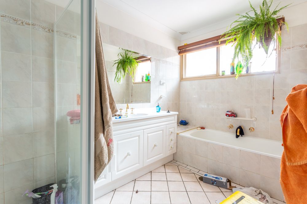 Bathroom with white bathtub, sink, and tiles. Window with curtain, shower stall on left.