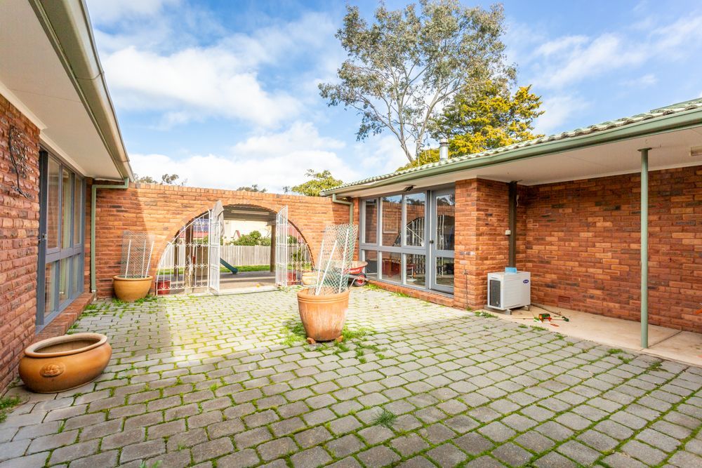 Brick courtyard with a tiled floor, potted plants, and arched entryways under a cloudy sky.