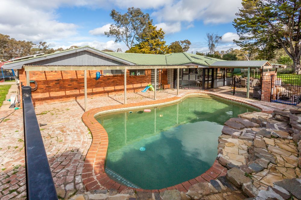 Swimming pool with brick surround, next to a brick house under a blue sky.