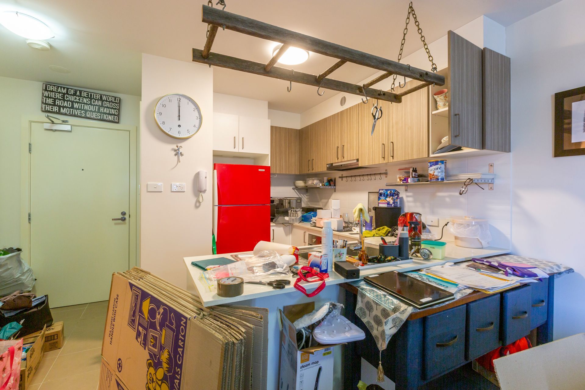 Kitchen with open cabinets, a sink, and a view into a messy living room with boxes and furniture.