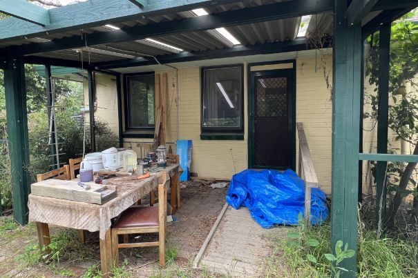 Cluttered dining room with table covered in clothes and items; two framed art pieces on the wall.