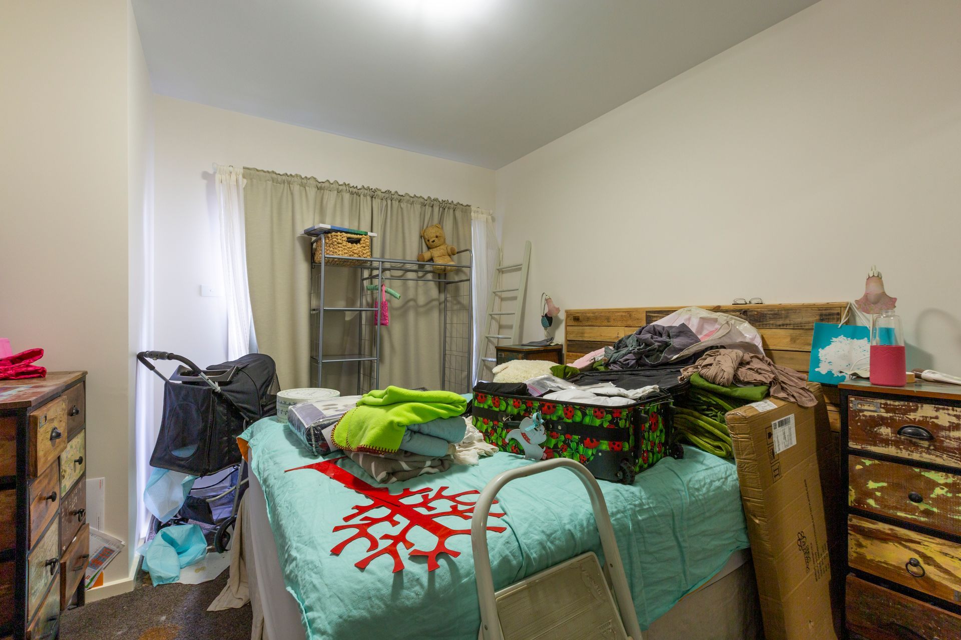Messy bedroom with clothes and items on the bed, furniture, and a clothing rack.