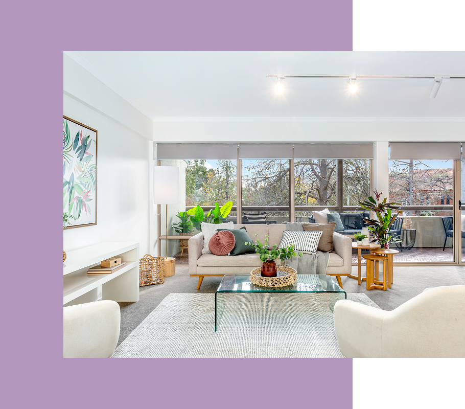 Living room with a sofa, glass coffee table, and large windows overlooking trees.