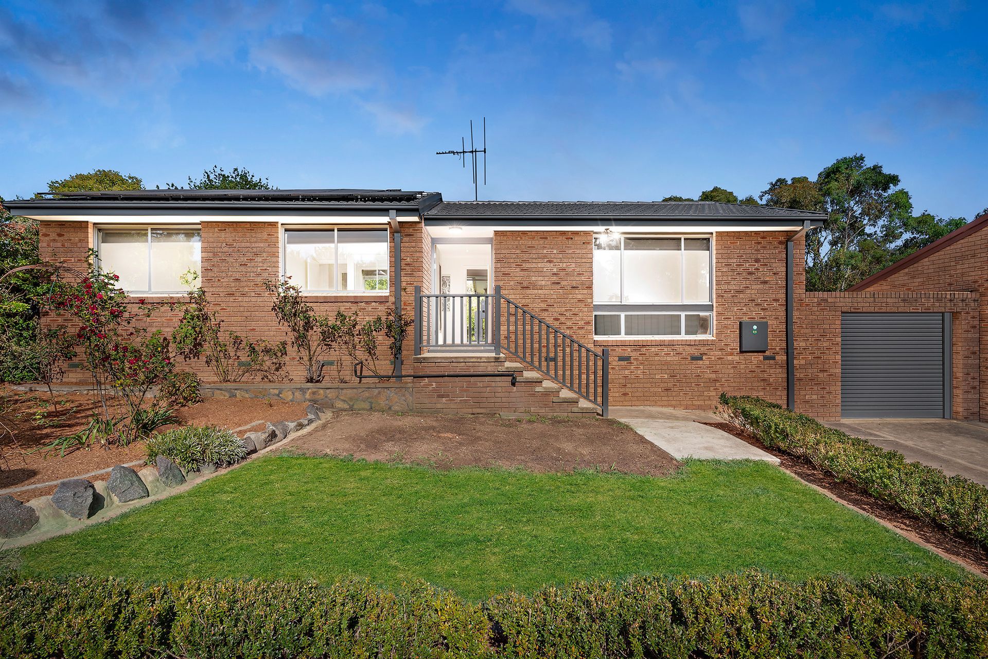 Brick home with a small lawn, steps to the front door, and a garage on a sunny day.