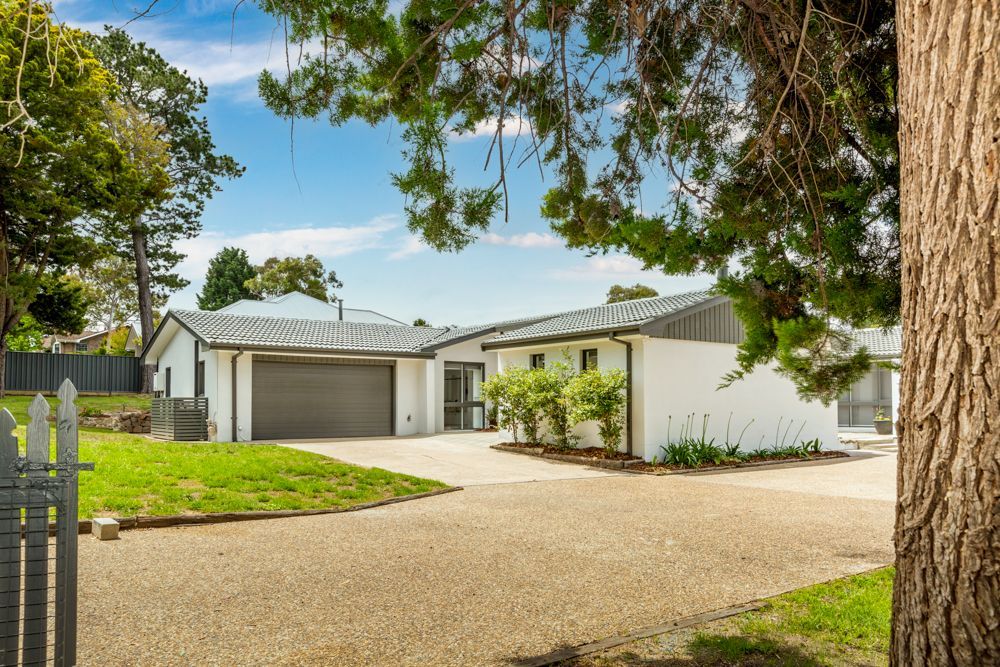White house with attached garage, gravel driveway, and trees.