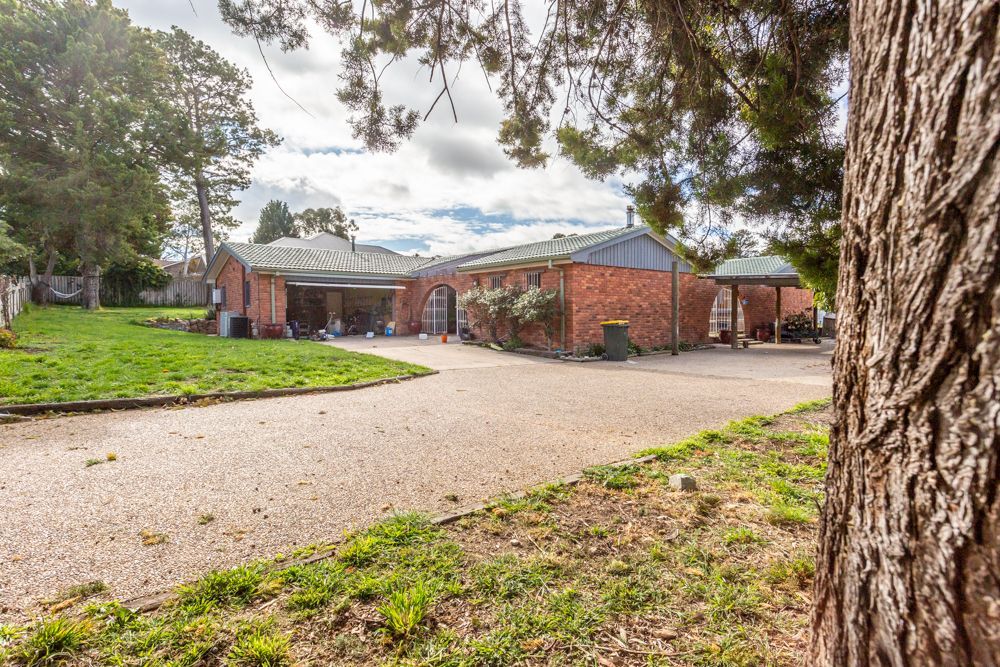 Gravel driveway leads to a brick house with a covered porch, set on a grassy lot under a cloudy sky.