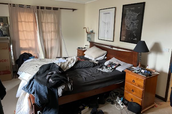 A cluttered bedroom with unmade bed, nightstand, posters, and curtains.