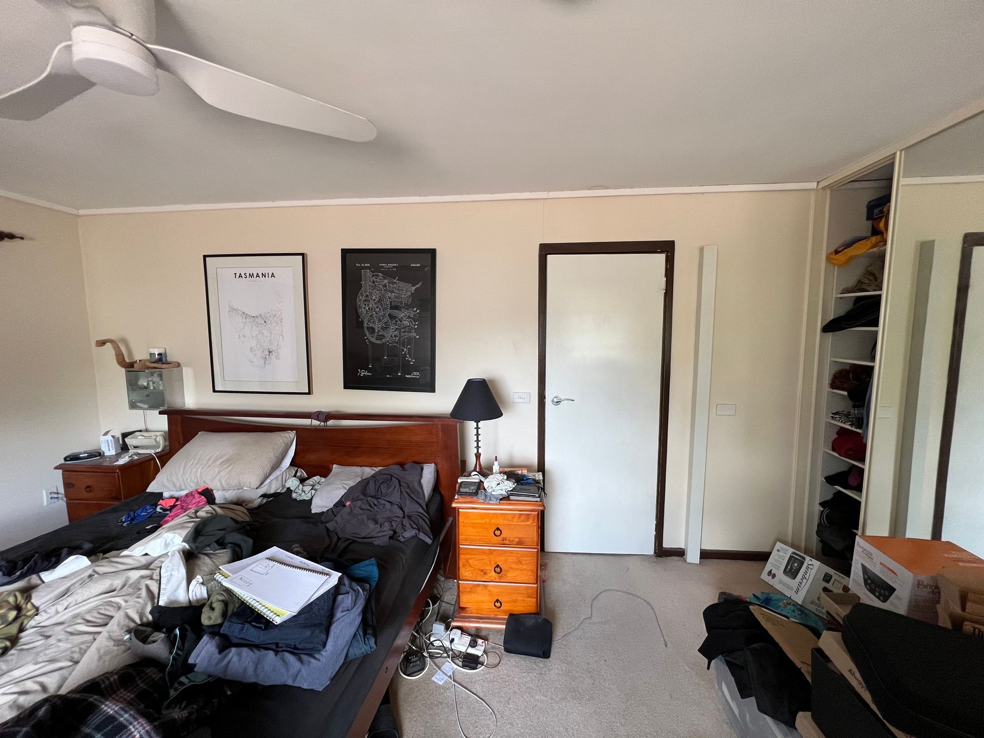 Cluttered dining room with table covered in clothes and items; two framed art pieces on the wall.