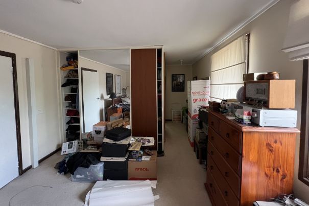 Cluttered room with shelves, chest of drawers, and various electronic items. Neutral color palette.