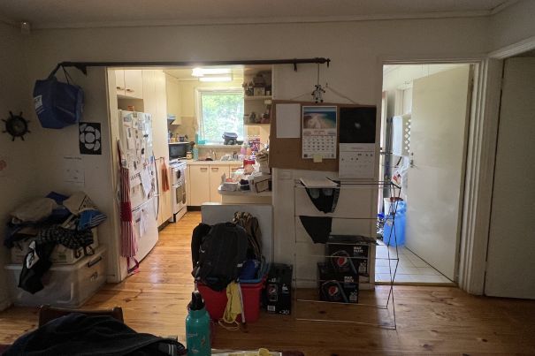 A cluttered interior with a kitchen, hallway, and various storage items against wooden floors.