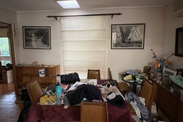 Cluttered dining room with table covered in clothes and items; two framed art pieces on the wall.