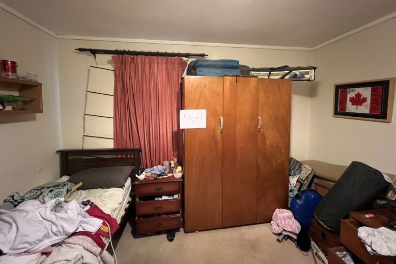 Cluttered bedroom with a bed, wardrobe, and items strewn about. A Canadian flag hangs on the wall.