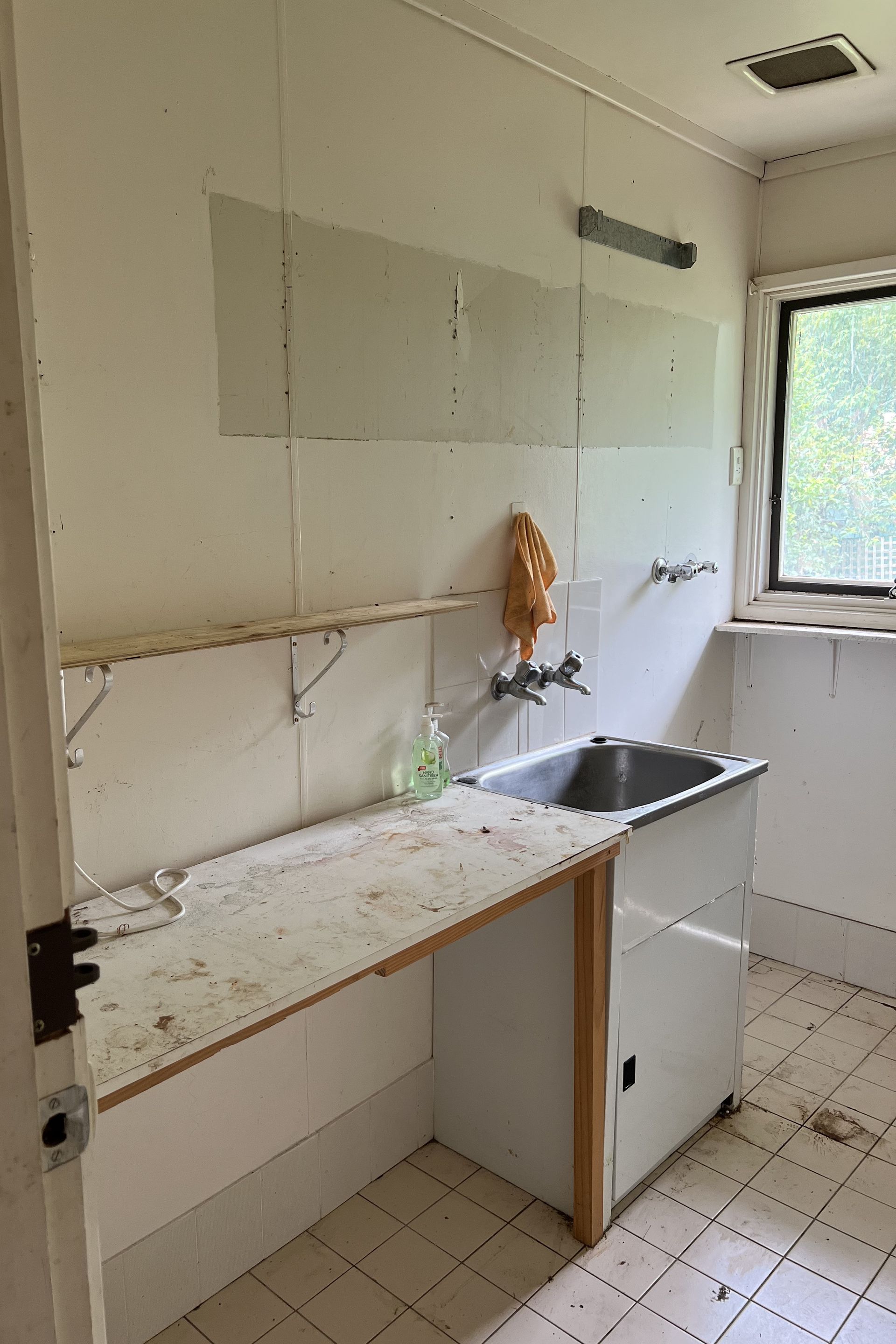 Dilapidated utility room with a sink, counter, and peeling wallpaper.