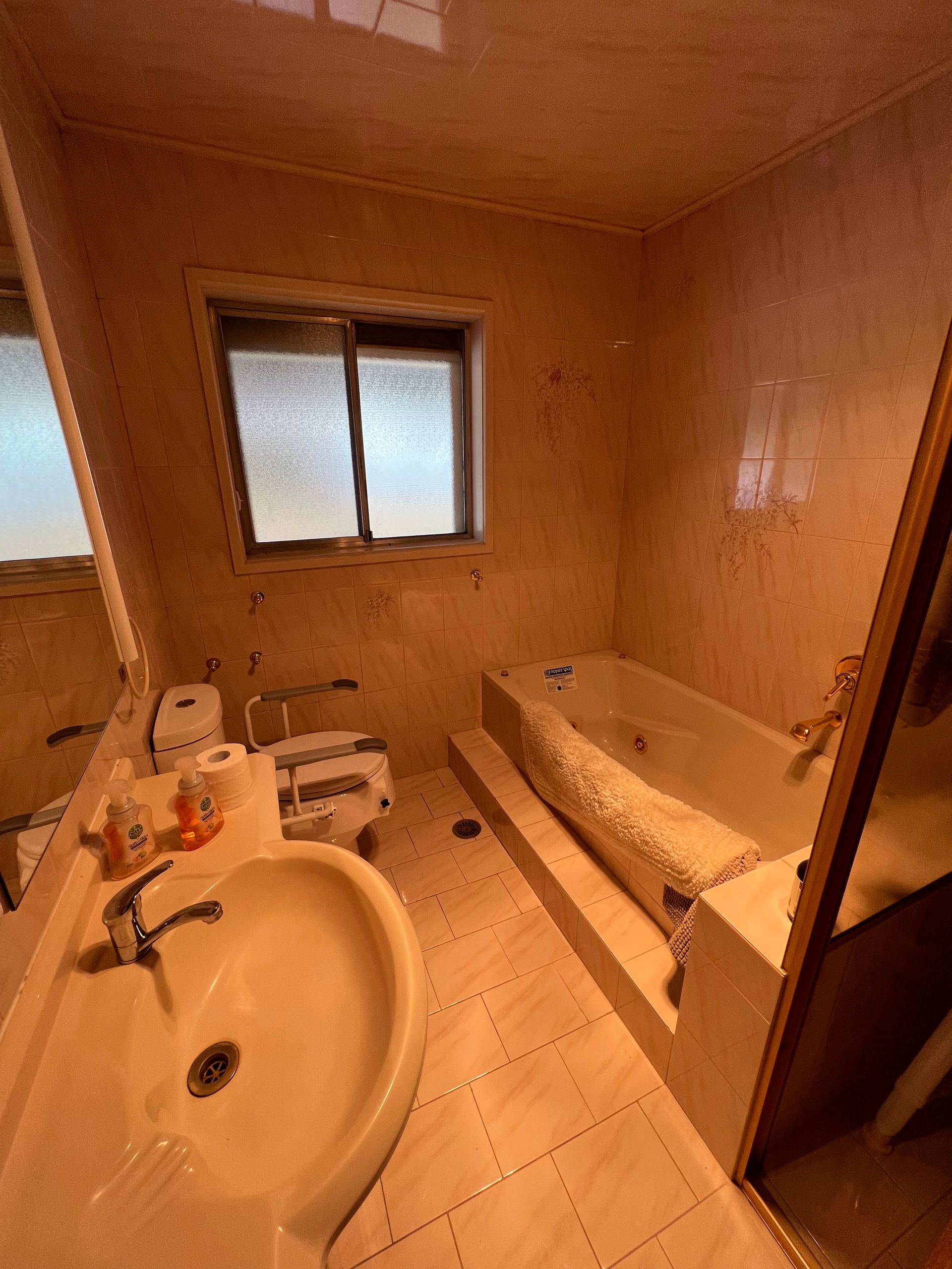 Bathroom with tub, sink, toilet, and window. Tile walls and floor, neutral tones.