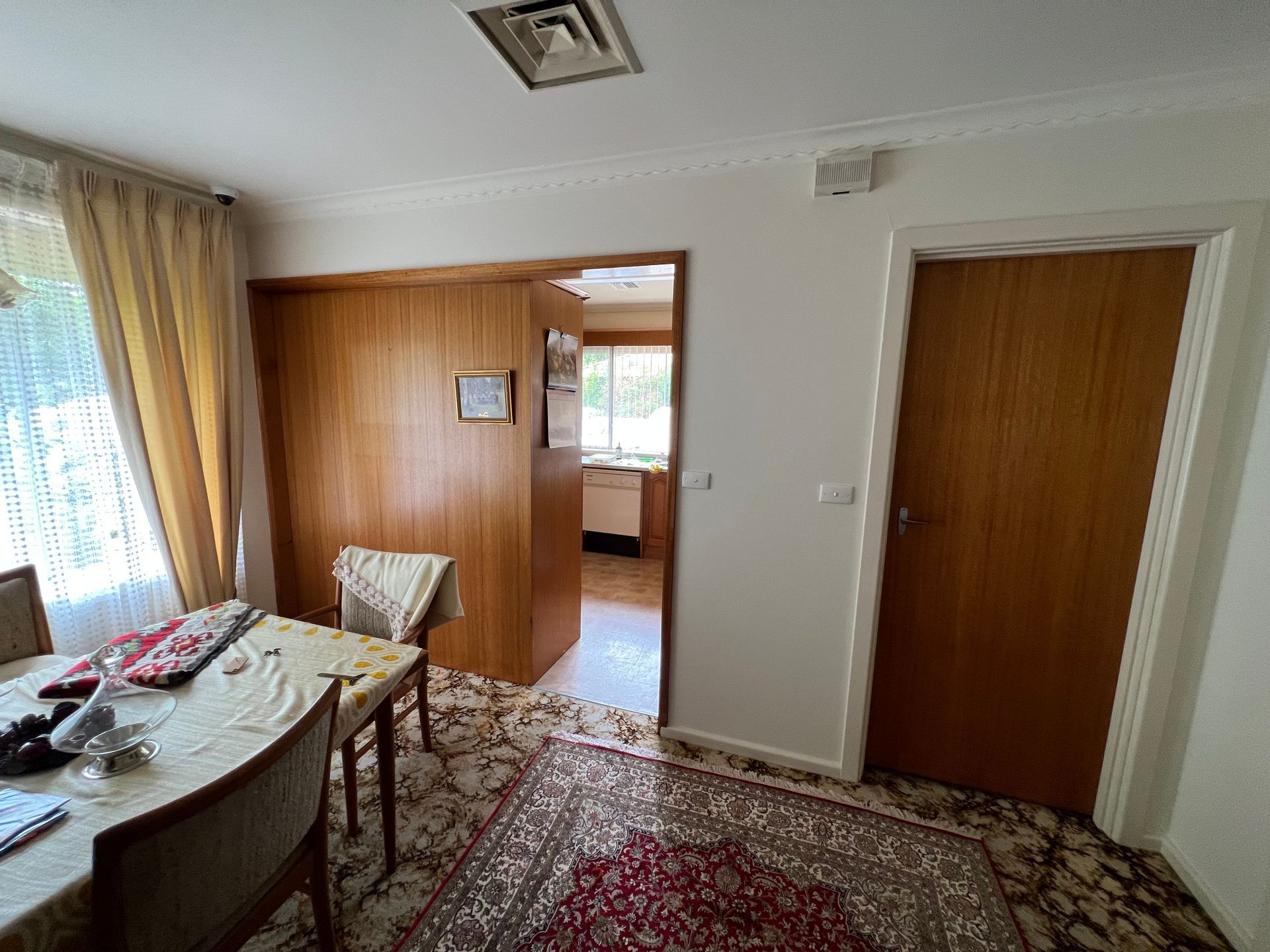 Dining room with table, chairs, wood paneling, doorway to kitchen, and floral rug.