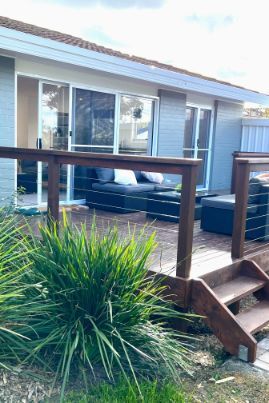 Wooden deck with dark gray outdoor furniture in front of a light gray house with sliding glass doors.
