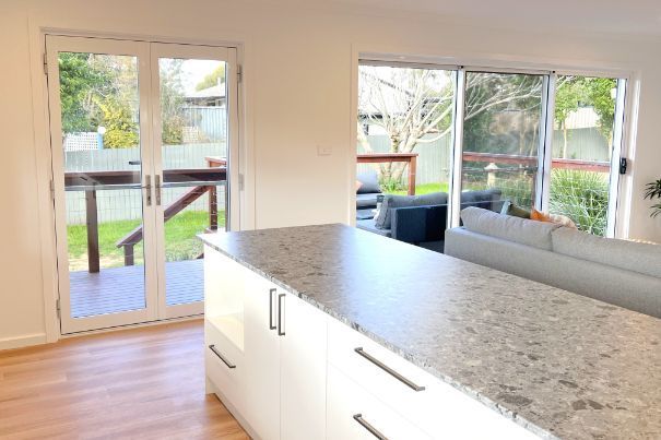Kitchen with white cabinets, gray countertop, and access to a deck and backyard via glass doors.