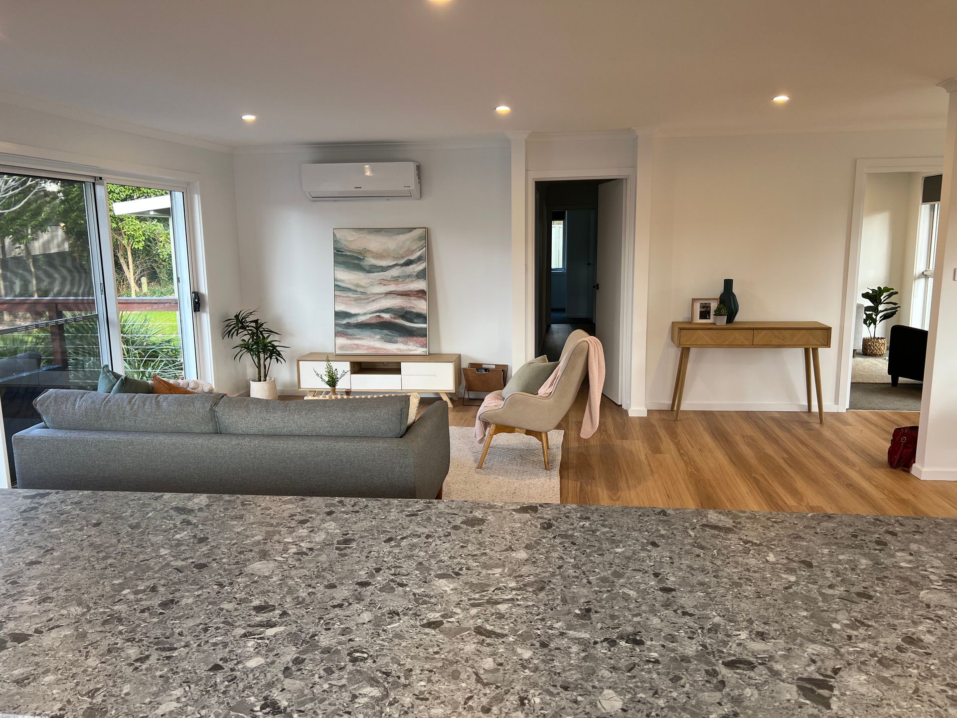 Living room with gray sofa, chair, and wooden floor; artwork and a small table are present.