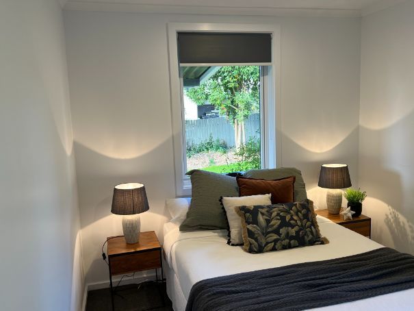 Bedroom with bed, nightstands, lamps, and a window overlooking greenery. White walls.