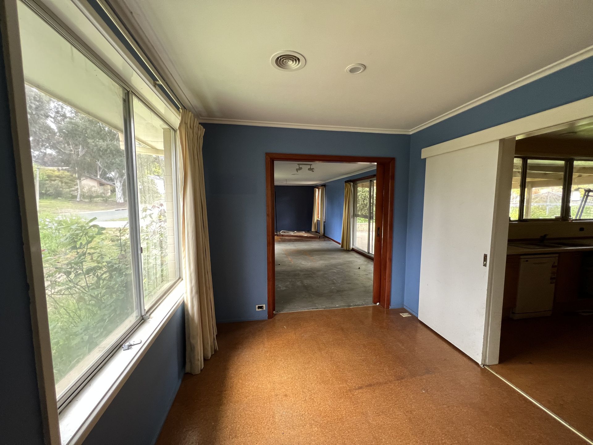 Interior view of a room with blue walls, a brown floor, and large windows looking outside.