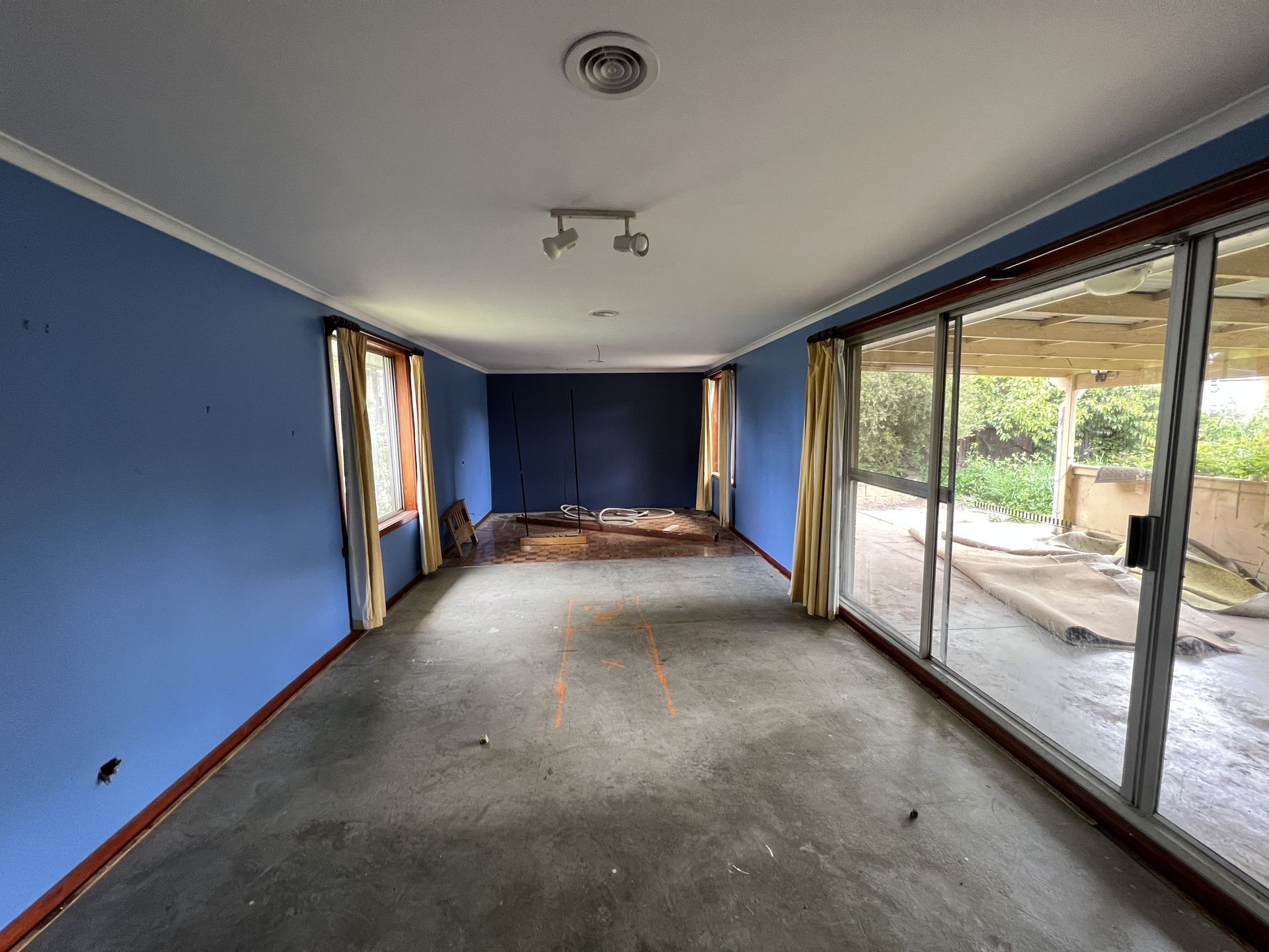 Empty room with blue walls, sliding glass door, and worn flooring.
