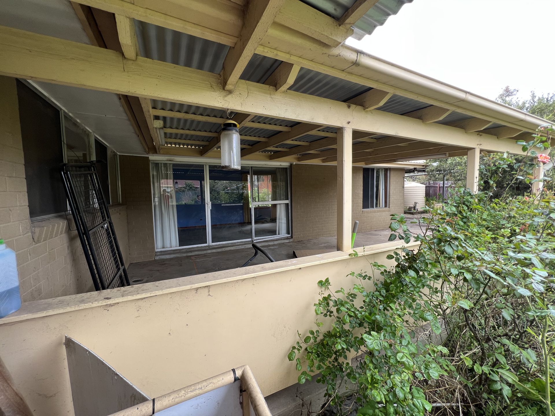 Covered patio with a low wall, corrugated metal roof, and a view of a house.
