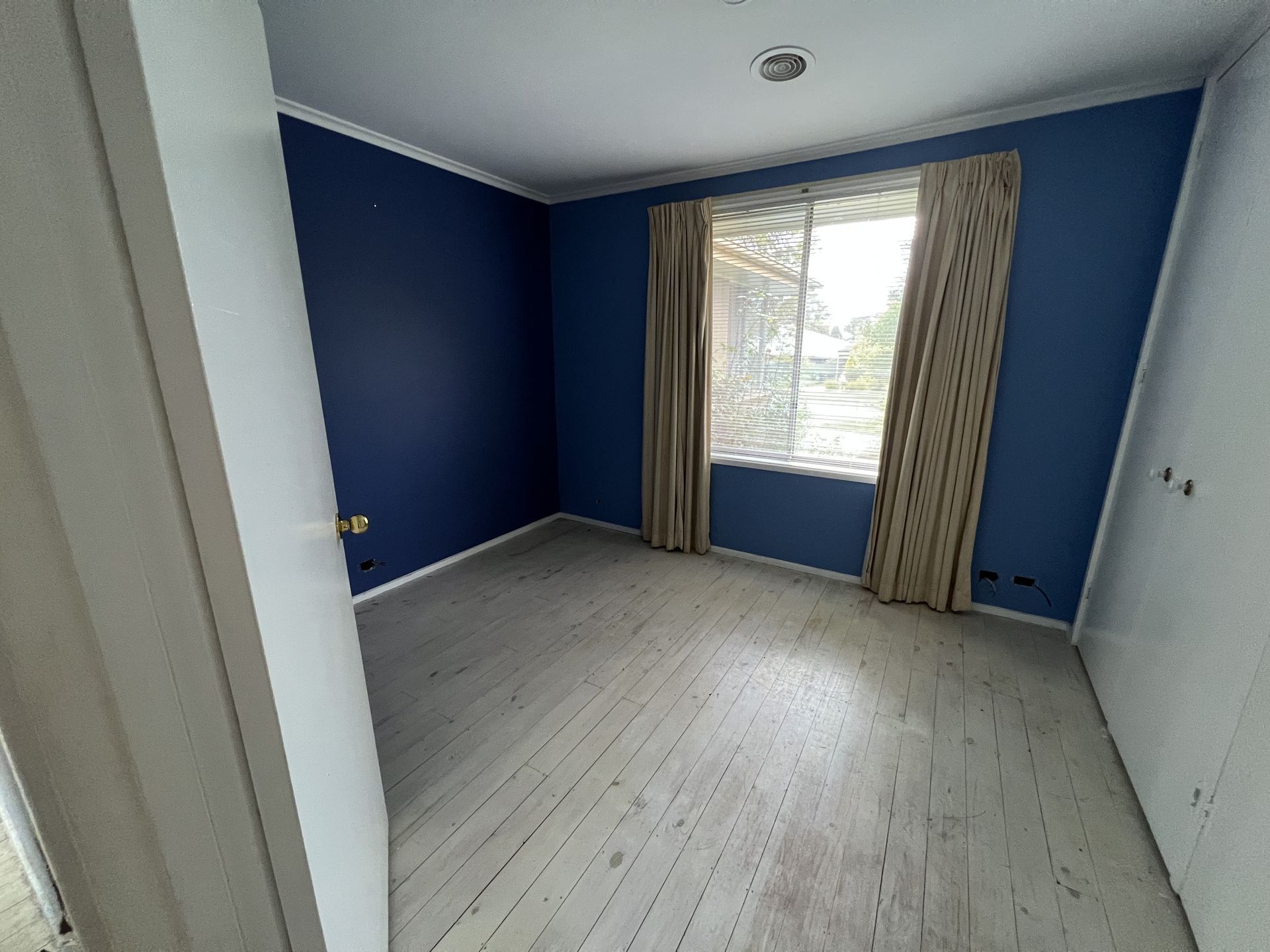 Interior view of a room with blue walls, a brown floor, and large windows looking outside.