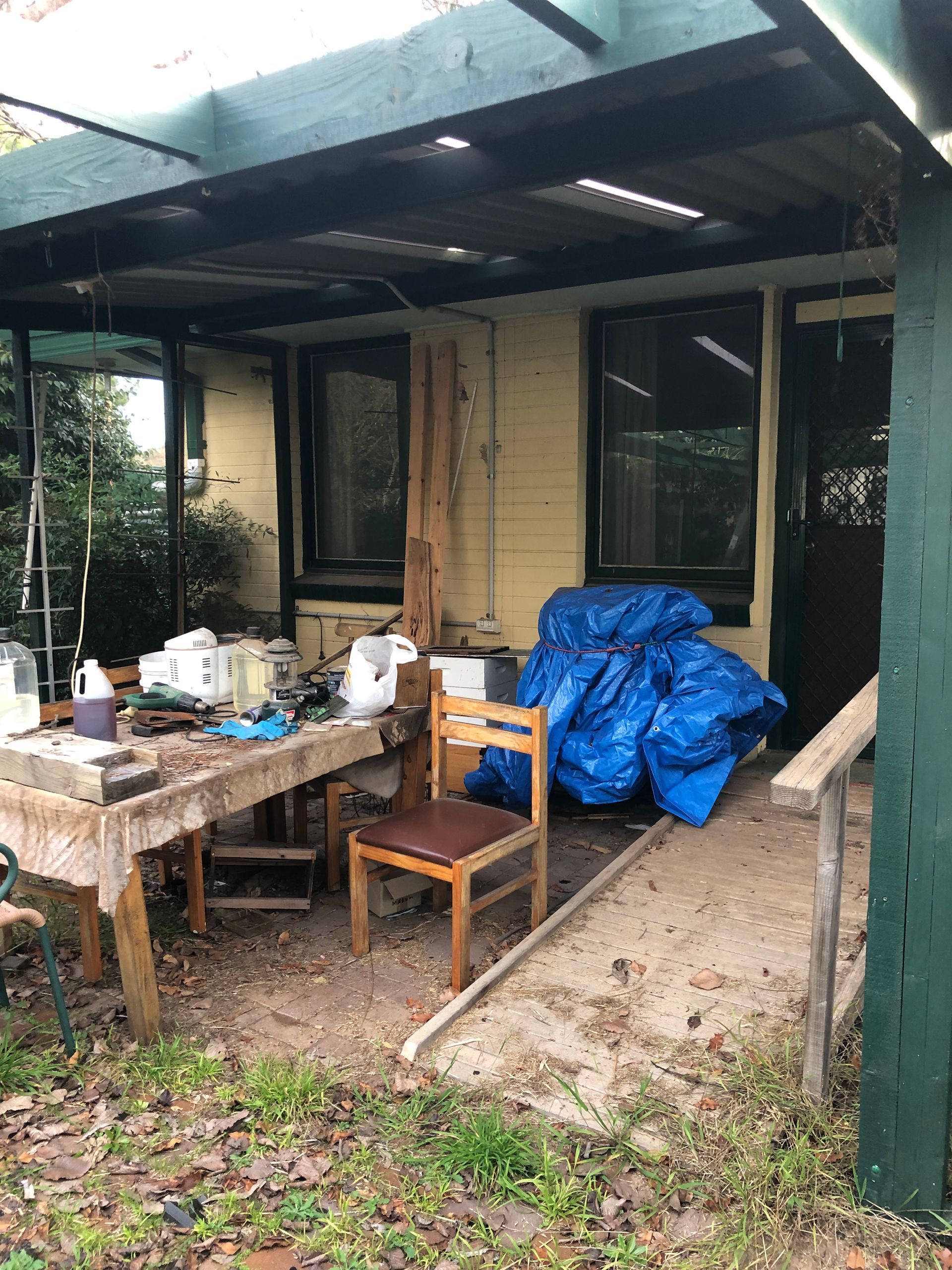 Messy bedroom with wardrobe, dresser covered in clothes, fan, and cluttered floor.