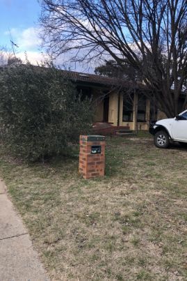 Messy bedroom with wardrobe, dresser covered in clothes, fan, and cluttered floor.