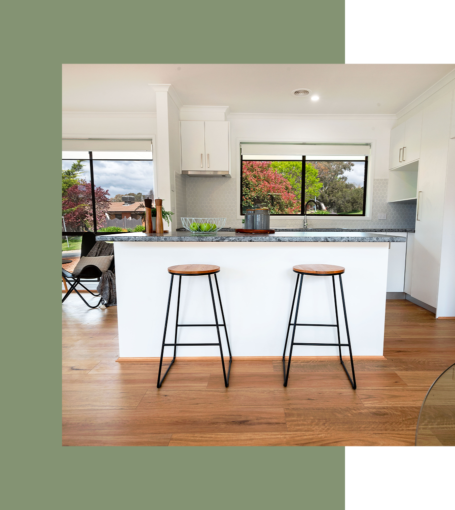Kitchen with granite countertop, white cabinets, two stools, and large windows.