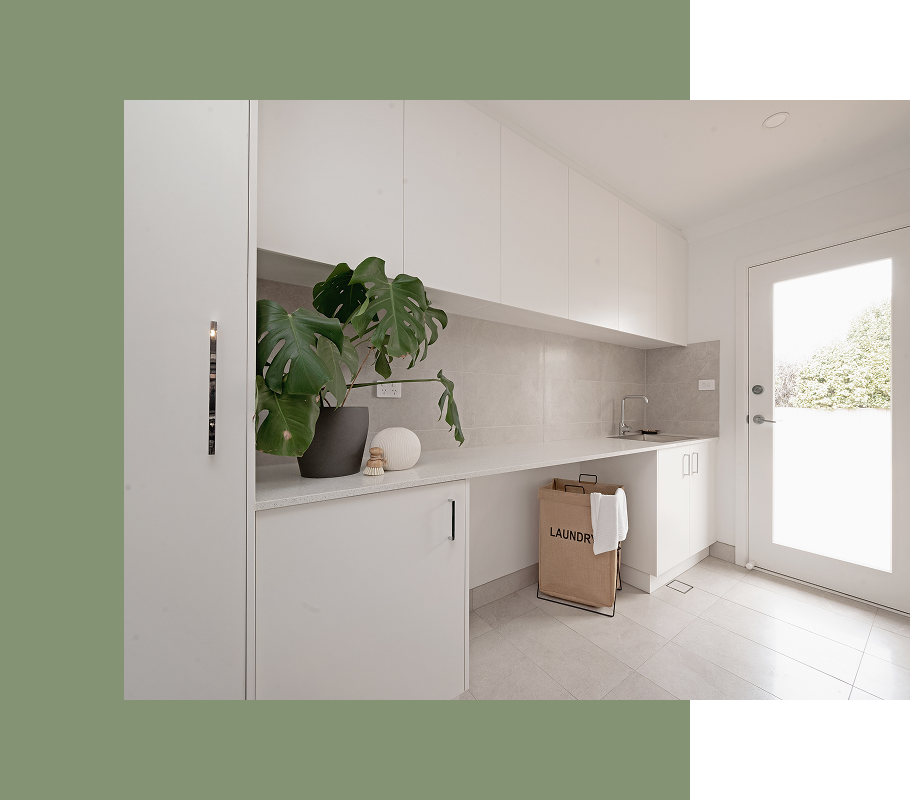 Laundry room with white cabinets, countertop, sink, and a large potted plant. Door on the right.