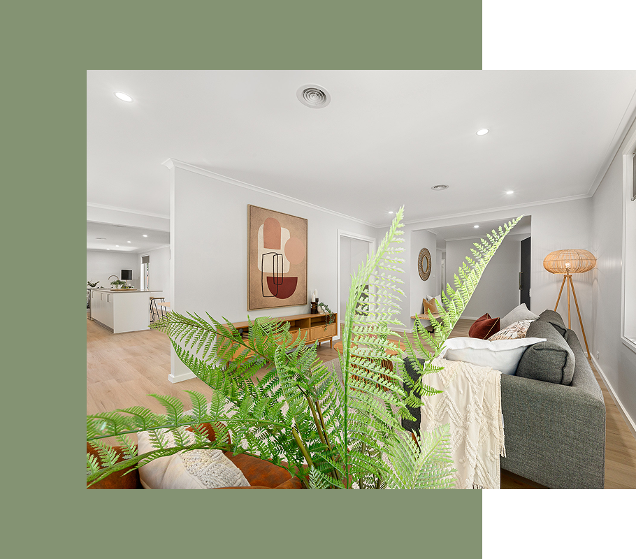 Living room with green plant, grey couch, artwork, and light wood floor.