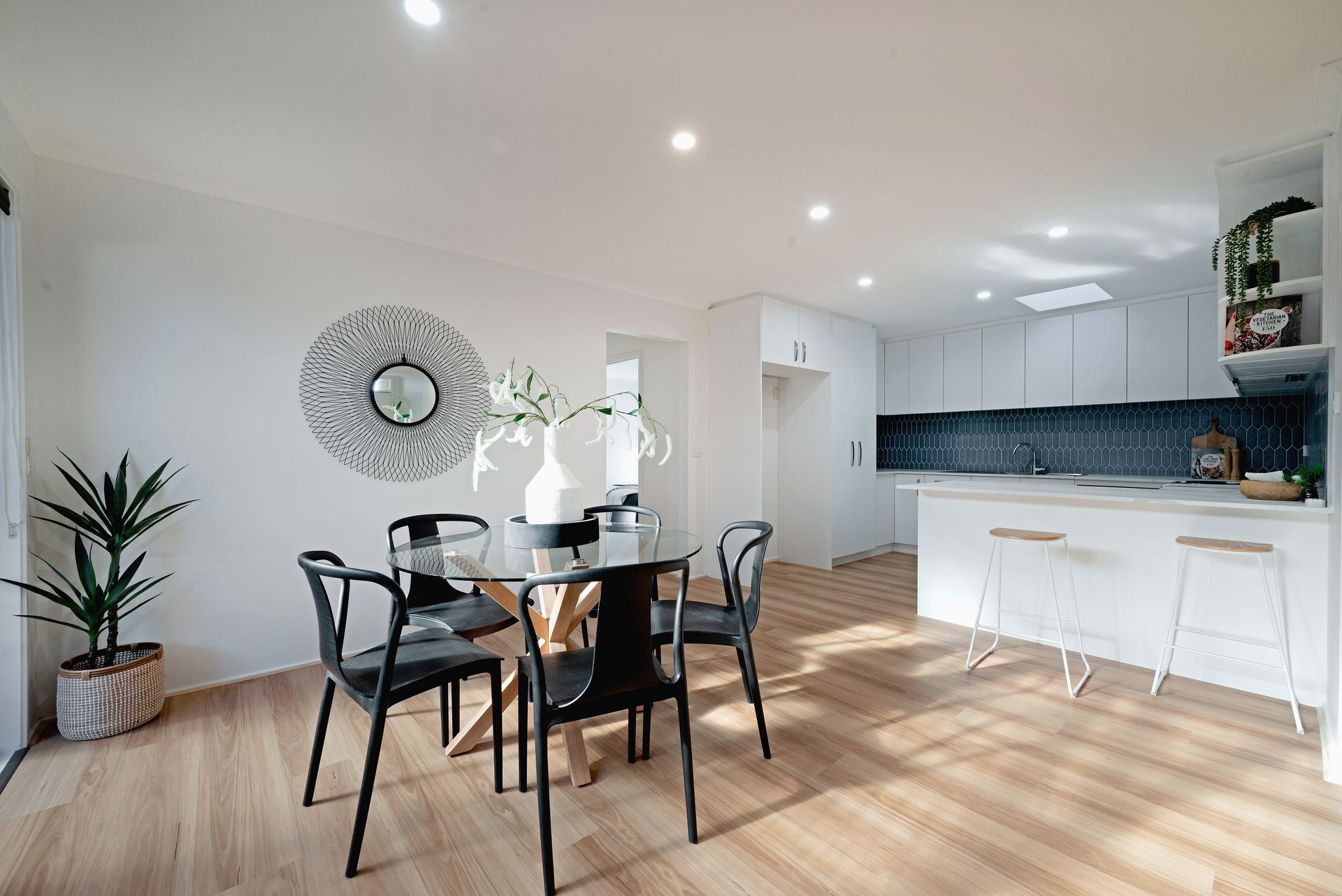 Dining area with table, chairs, and open kitchen, featuring white walls and wooden floors.