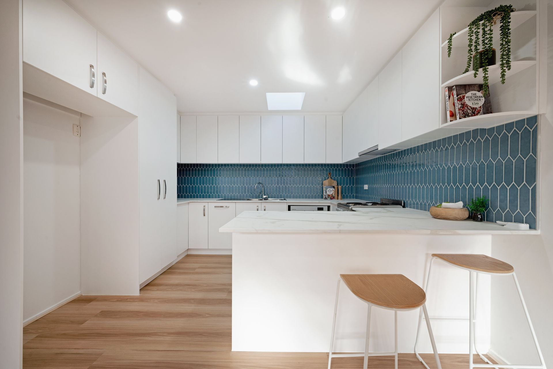 Modern white kitchen with teal backsplash, island, wooden floors, and two bar stools.