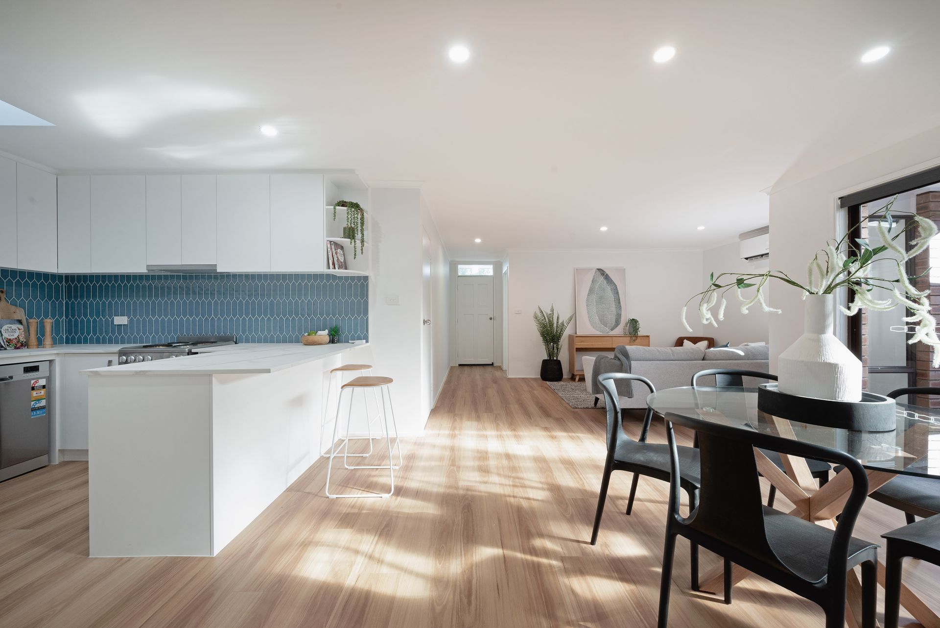 White laundry room with sink, counter, cabinets, and door to outside. Plant and laundry basket are present.
