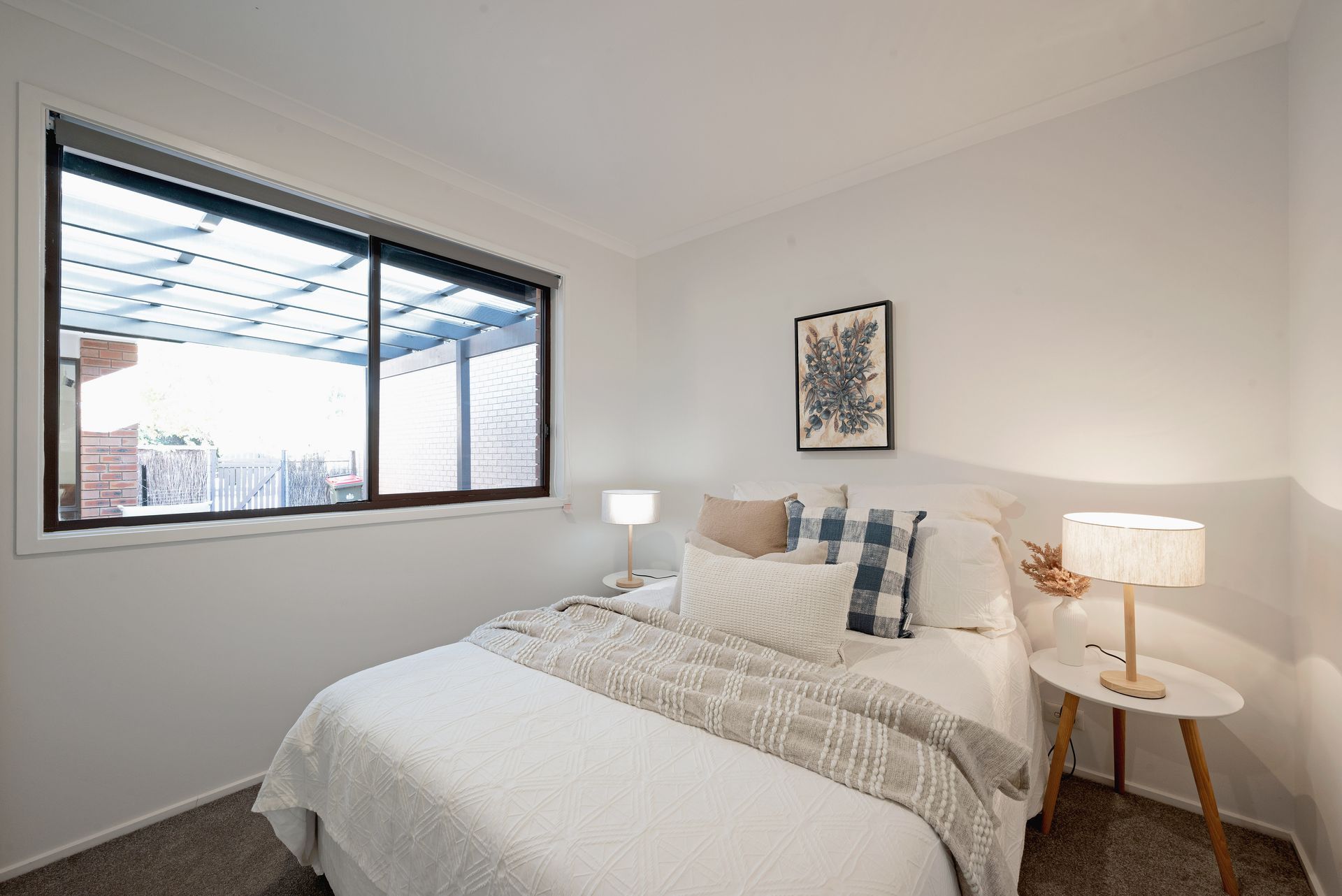 Bedroom with a bed, small table, lamp, window, and wall art.