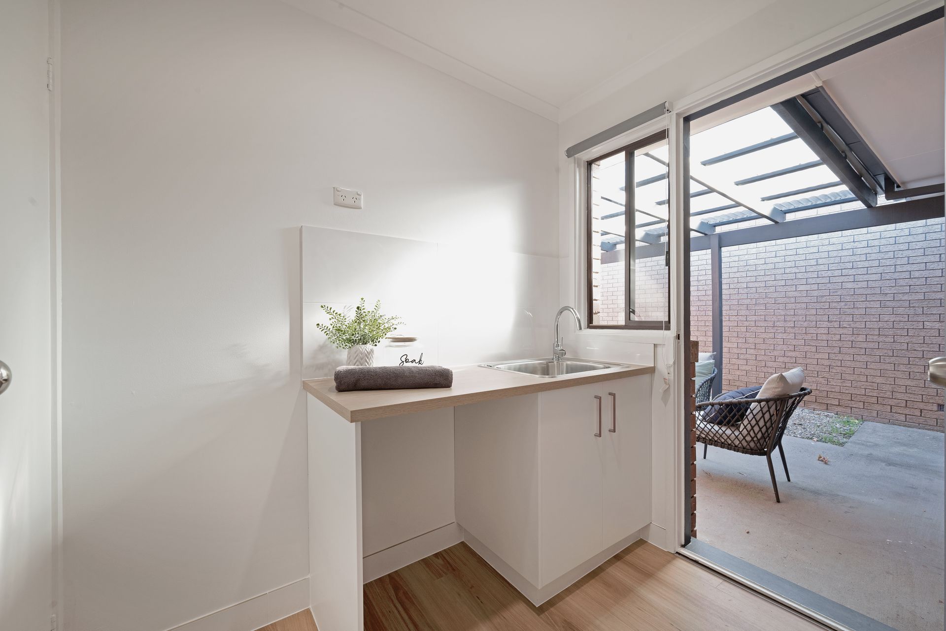 Laundry room with white cabinets, sink, and sliding door to patio with chair.