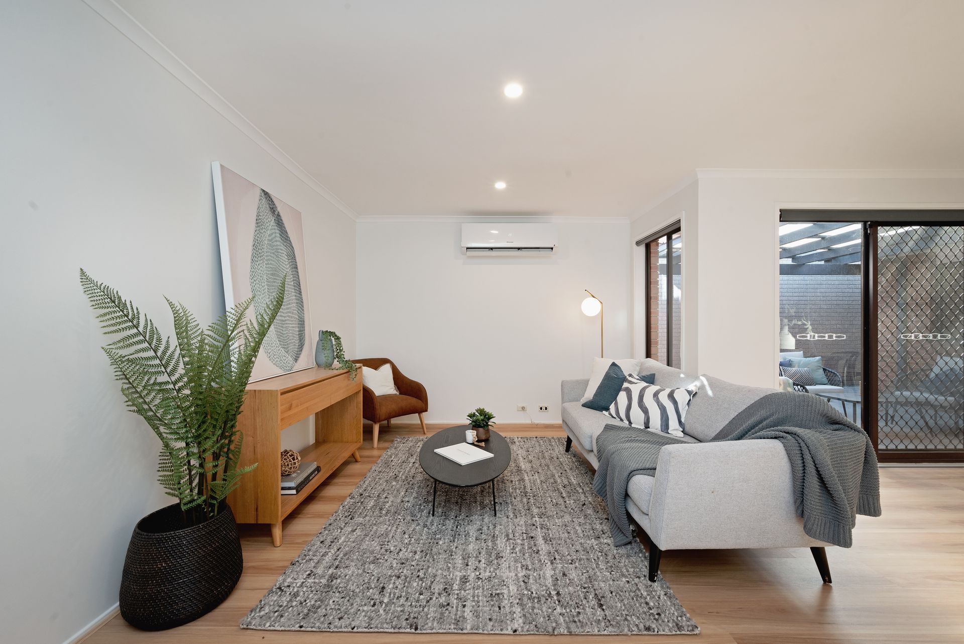 Living room with gray sofa, rug, and wooden furniture, next to sliding door.