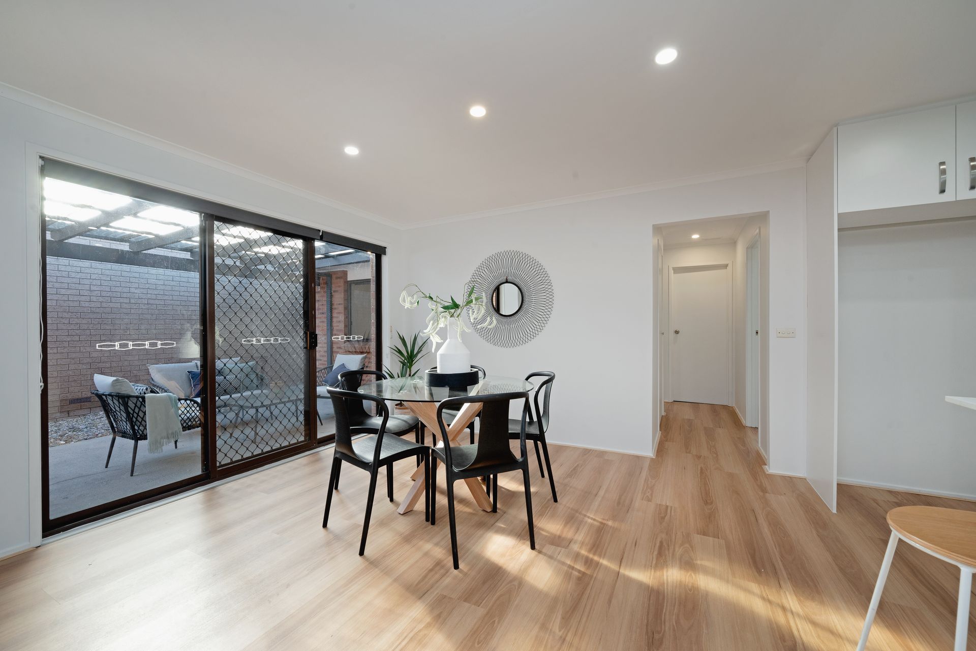 Dining room with black table and chairs, sliding door to patio, wood floors, and decorative mirror.